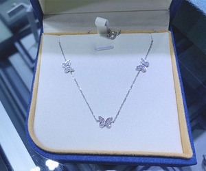 Macro detail of silver butterfly necklace with three crystal-encrusted charms in a blue box