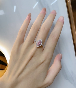 Gros plan d'une bague marquise avec diamant rose et serti halo sur le doigt du modèle