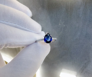 Macro shot of pear cut blue sapphire ring with a silver band and side diamonds