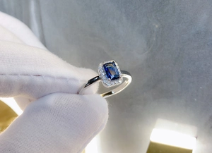 Detailed macro shot of rectangular blue zircon halo ring with silver band held in hand