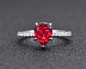 Macro shot of silver ring with pear-shaped red gemstone and pavé-set side stones