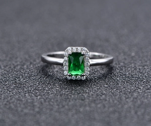 Macro shot of emerald-cut green gemstone ring with sparkling diamond halo and silver band