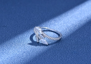 Macro detail of silver leaf ring featuring marquise-cut stones on a textured blue surface
