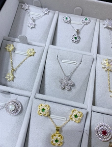Détail de colliers et boucles d'oreilles floraux argentés et dorés dans un plateau gris