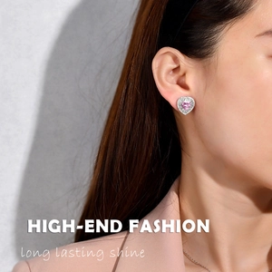 Close-up of heart-shaped pink diamond earrings with silver halo on a model's ear