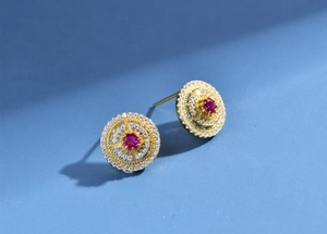 Close-up of gold plated round earrings featuring a red ruby center and pavé diamonds
