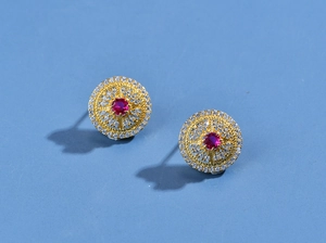 Detail view of gold earrings with red ruby center and white diamond halo on blue background