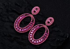 Close-up of luxury rose gold oval drop earrings with pink gemstones on a dark stone background
