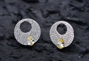 Macro detail of silver round earrings with pear-cut yellow stones on dark rock