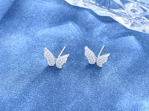 Dettaglio orecchini a farfalla con cristalli scintillanti su velluto blu elegante