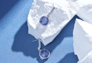 Macro detail of round blue gemstone earrings with zircon halo on white stone surface