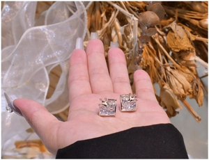 Close-up of square carbon diamond earrings with crown details on a hand-held display