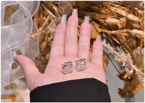 Detailed view of square silver heart crown stud earrings held in a hand for scale