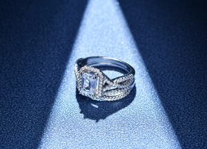Détail d'une bague taille émeraude avec halo de diamants et anneau pavé entrelacé