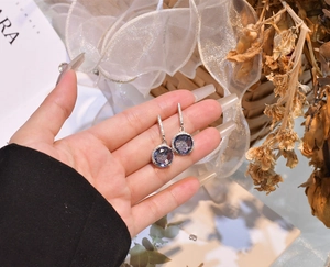 Detailed view of round 11mm purple gemstone earrings with halo diamonds in silver setting