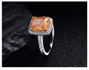 Macro shot of a radiant cut orange gem ring with a halo of diamonds and silver band