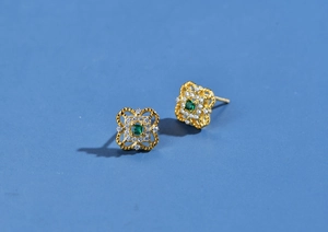 Close-up of gold clover stud earrings featuring emerald-cut green stone and diamonds