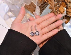 Detail of 11mm purple zircon sterling silver earrings held by hand against floral background