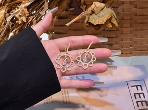 Detailed shot of golden hollow flower earrings with pear-cut crystals held by hand