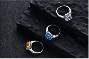 Radiant cut 925 silver rings with orange, blue, and clear gemstones on dark rock