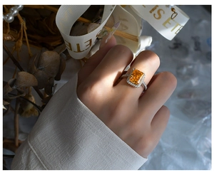 Close-up of 8x10mm radiant cut orange gemstone ring with halo diamonds on a silver band