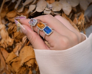 Macro shot of three 925 silver halo rings with radiant cut orange, blue and white stones