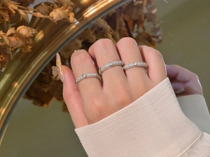 Trois bagues en argent 925 serties de diamants pavés présentées sur main avec reflet miroir