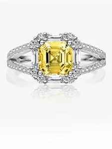 Close-up of a silver ring featuring a large square yellow stone and side diamonds