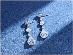 Macro detail of pear-shaped drop earrings with white zircons on blue sand texture