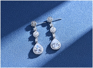 Macro detail of pear-shaped silver drop earrings with sparkling cubic zirconia on blue base