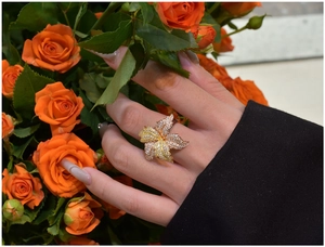 Close-up of a floral leaf ring with sparkling pavé diamonds worn with orange roses