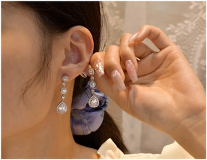 Detail of silver pear-shaped drop earrings with halo-set zircons on female model
