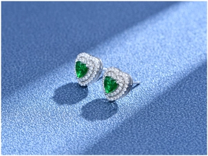 Macro detail of heart-shaped emerald stud earrings with double halo zircon setting