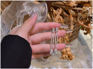 Macro detail of long silver drop earrings with pavé crystals and knotted tassels design