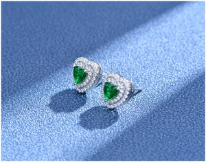Macro shot of heart-shaped emerald stud earrings with double halo diamond setting in silver