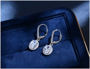 Close-up of oval cut gemstone earrings with micro-pave diamonds in a navy velvet box