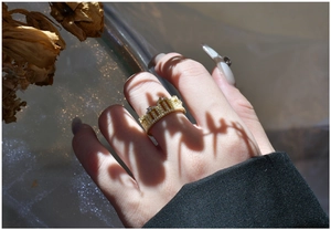 Detail of elegant gold crown ring with white zircon stones worn on hand with floral shadow