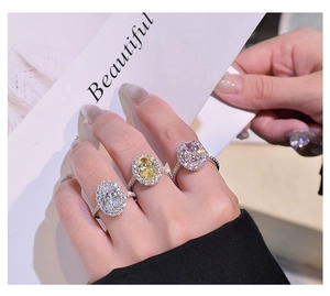 Detailed view of three halo-set oval rings in white, yellow, and pink colors worn by model