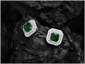Detailed view of square emerald earrings with double halo pavé diamonds on dark rock