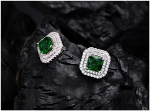 Macro shot of square emerald earrings with double halo diamond accents on black rock