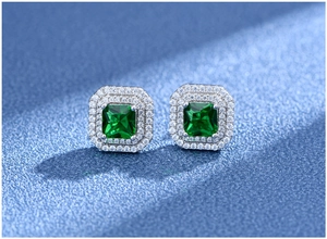 Macro shot of square emerald earrings with double halo of white stones on blue surface