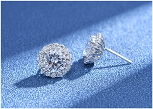 Macro shot of silver halo stud earrings with round brilliant-cut stones on blue texture