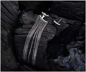 Macro detail of asymmetric silver tassel earrings with micro-set zircons on dark stone