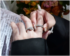 Close-up of S925 silver halo square ring and pavé band set on a vintage book page