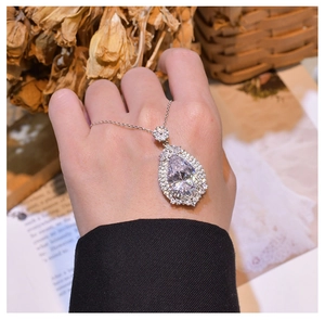 Macro detail of pear-cut waterdrop pendant with halo diamond setting on hand