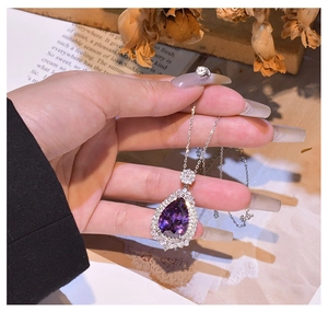 Macro shot of silver pear-cut purple gemstone pendant with diamond halo setting