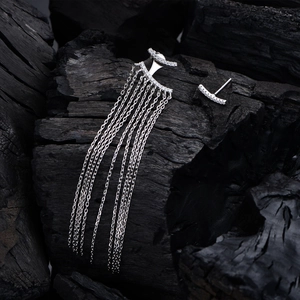 Asymmetric long tassel silver earrings with sparkling cubic zirconia on dark wood
