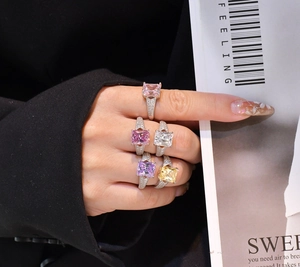 Nahaufnahme von fünf bunten Ringen mit Prinzess-Schliff auf der Hand über einem Magazin