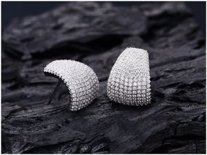 Macro shot of curved pavé-set zirconia earrings on textured black charcoal background