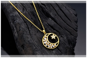 Macro shot of gold moon and star necklace with shimmering crystals on dark stone